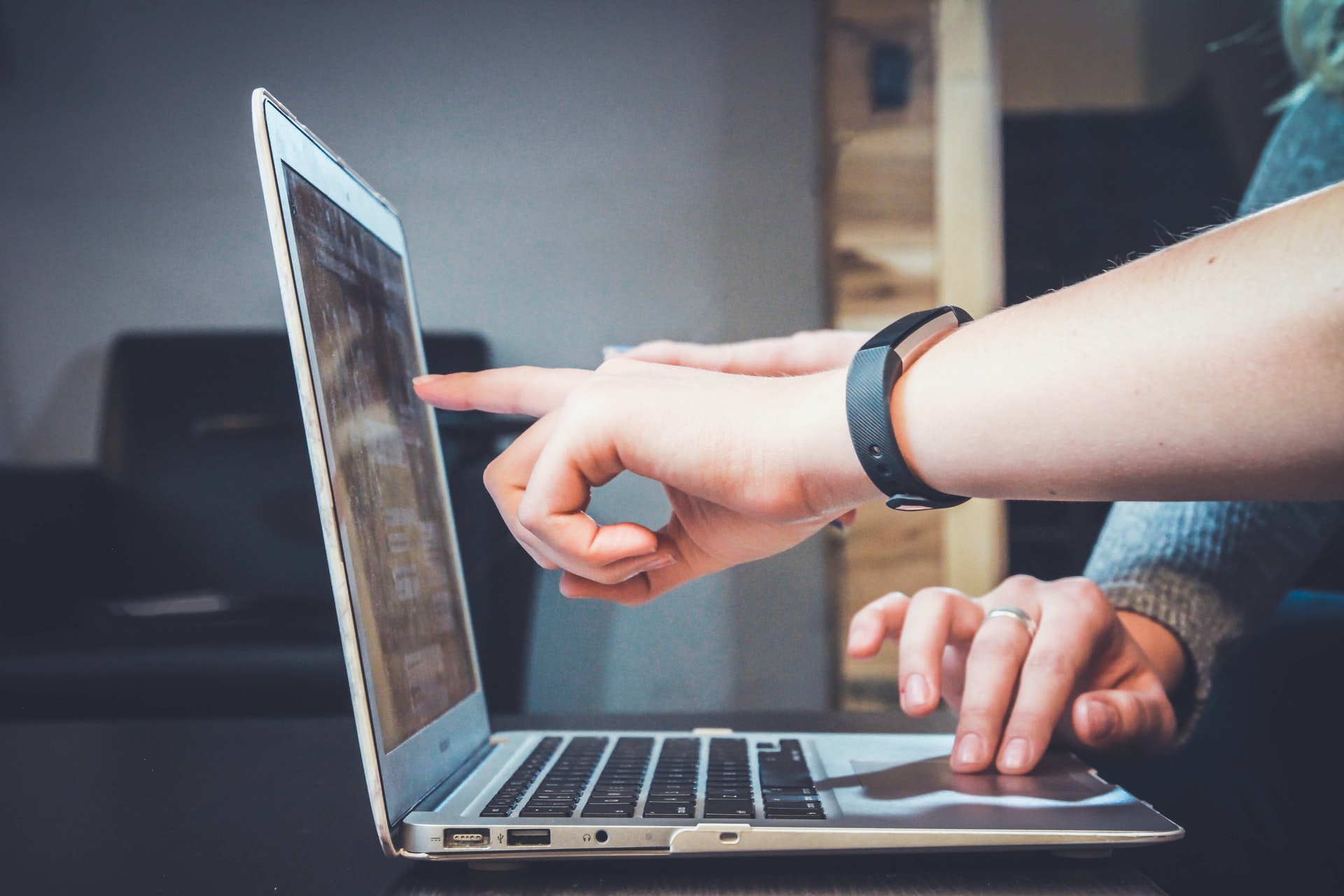 Person with black watch pointing at laptop